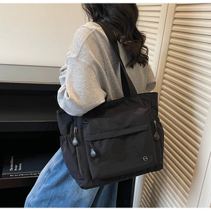 Détail du sac cabas en nylon noir avec poches zippées et logo de la marque CM rond