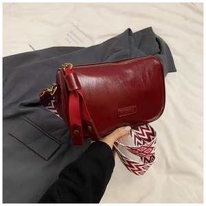 Close-up of burgundy pillow bag with geometric wide strap and gold hardware accents