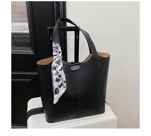 Detail of black lychee grain leather tote bag with printed silk scarf on a suitcase