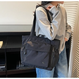 Détail du grand sac cabas noir en nylon avec plusieurs poches et anses en tissu sur modèle