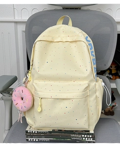 Detail of cream canvas backpack with colorful dots and a plush donut charm accessory