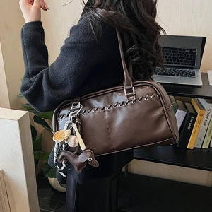 Detalle de bolso Boston retro marrón oscuro con ojales y colgantes de tema deportivo