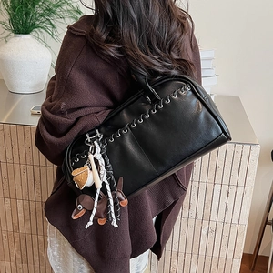 Detalle del bolso de cuero negro con ojales metálicos y dijes de perro de peluche