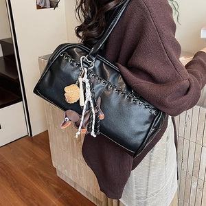 Detalle de bolso de hombro en cuero negro con colgantes de teckel y croissant al lado