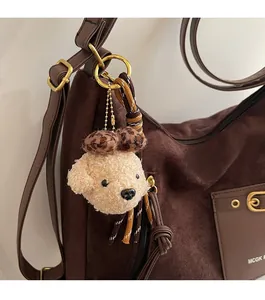 Gros plan d'un pendentif chien en peluche beige avec nœud léopard sur un sac fourre-tout brun