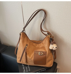 Detail of a brown suede tote bag with metal zipper and cream plush bear keychain