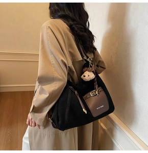 Détail du sac cabas en toile noire avec poche en cuir marron et pendentif ours mignon