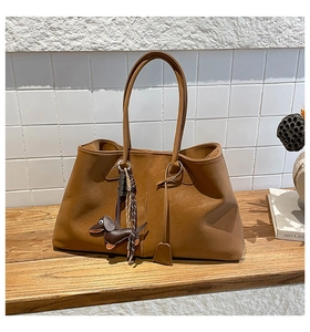 Detail einer braunen Leder-Tote-Bag mit Dackel-Anhänger und gewebtem Zubehör-Element
