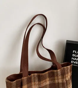 Detail of a brown plaid tote bag featuring a thick, smooth fabric shoulder strap