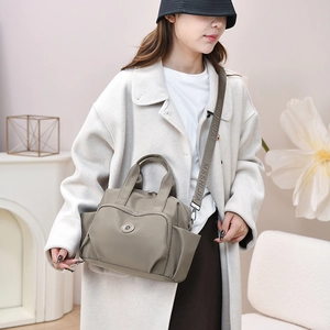 Detail of grey-green nylon crossbody bag with multiple zipper pockets and wide letter strap
