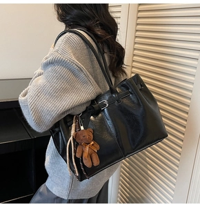 Detail of black faux leather tote with silver metal buckle and brown plush bear charm