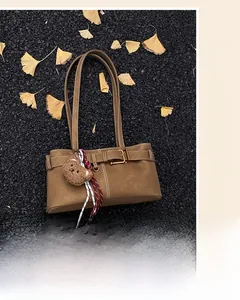 Brown leather underarm bag with metal buckle and teddy charm on ginkgo leaf ground