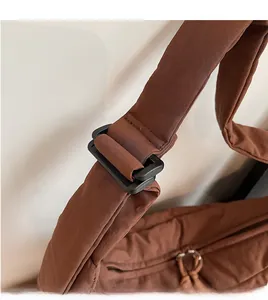 Detail of adjustable long shoulder strap with black buckle on brown quilted puffer bag