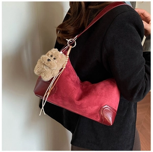 Detail of dark red suede underarm bag with teddy bear charm shown on model's shoulder