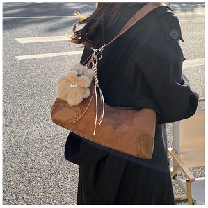 Detail of a brown suede baguette bag with a plush bear charm on a slim leather strap