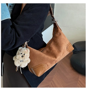 Detail of a brown suede hobo bag with a plush bear charm shown on a model