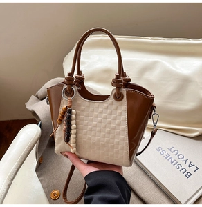 Détail du sac seau bicolore avec texture tissée beige et pendentif en perles de bois