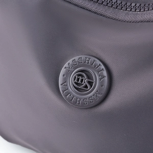 Close-up of charcoal nylon fabric texture with MSSHIJIA rubber logo and zipper detail
