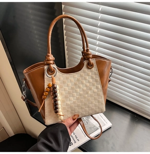 Détail d'un sac seau en cuir marron avec texture à carreaux et breloque à pompon