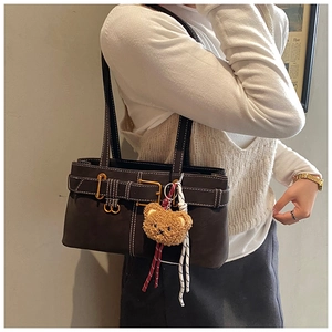 Detail of dark brown shoulder bag with gold hardware and a cute plush bear charm