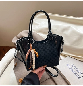 Détail du sac à main noir avec motif à carreaux, pompon en perles et bandoulière