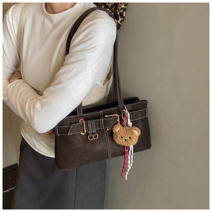 Close-up of brown leather underarm bag featuring a gold ring buckle and a cute bear charm