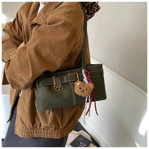 Close-up of olive green retro shoulder bag with metallic buckle and plush bear charm