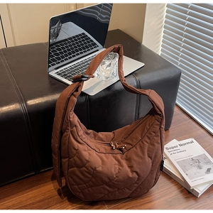 Sac bandoulière matelassé marron avec texture ondulée et cordon de serrage sur un banc