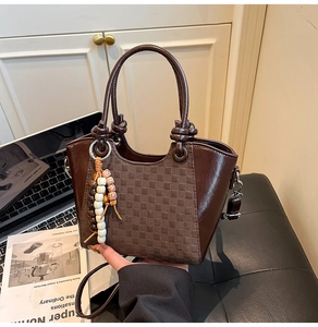 Détail d'un sac cabas marron foncé à damier avec breloque perlée et bandoulière