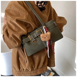 Detail of dark green shoulder bag featuring retro buckle and plush bear pendant