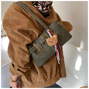 Detail of dark green shoulder bag with buckle strap and a brown plush bear charm