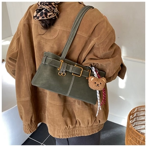 Detail of dark green matte shoulder bag featuring metal buckle and brown plush bear charm