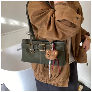 Detail view of dark green faux suede shoulder bag with bear pendant and buckle strap