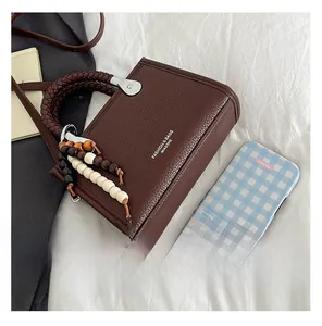 Detail einer dunkelbraunen Ledertasche mit geflochtenem Griff und böhmischem Perlenanhänger