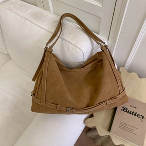 Close-up of brown suede tote bag featuring white stitching and adjustable metal buckle strap