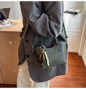 Détail d'un sac seau vert foncé avec texture tressée et charm perlé sur le côté