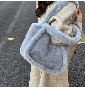 Detailed texture of a soft light blue faux fur tote bag worn with a beige winter coat