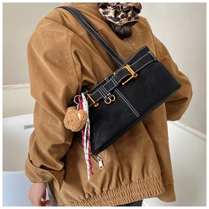 Side view of black underarm bag featuring white topstitching and cute bear charm pendant