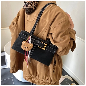 Detail of black suede tote bag with white stitching, gold buckle and plush bear charm