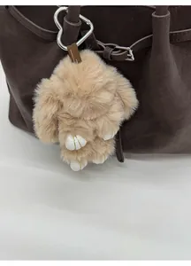 Close-up of khaki plush bunny charm with silver heart clip on a brown tote bag