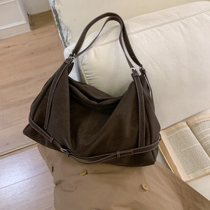 Detail view of large dark brown suede tote bag with contrast stitching on soft sofa