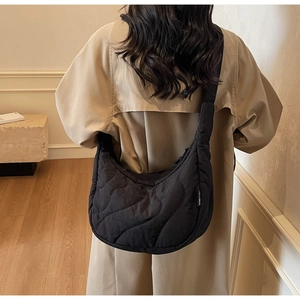 Détail du sac demi-lune noir matelassé avec coutures ondulées et petite étiquette tissée