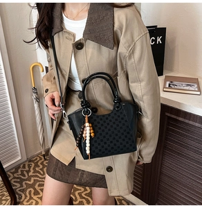 Détail du sac seau en cuir noir avec texture damier et pendentif en perles de bois