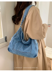 Detail of blue denim hobo bag with frayed edges worn by a model in a trench coat