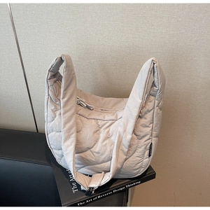 Gros plan du sac bandoulière matelassé gris clair sur un canapé en cuir