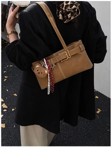 Brown leather underarm bag featuring a metal buckle and a cute teddy bear charm detail