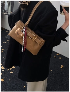 Brown leather shoulder bag with buckle detail and plush bear charm worn by a model