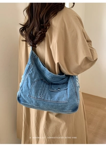 Detail of blue denim tote bag with layered pockets and frayed edges worn with a trench coat