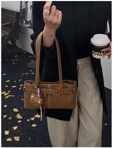 Brown leather underarm bag with gold buckle and bear charm on a model in autumn street