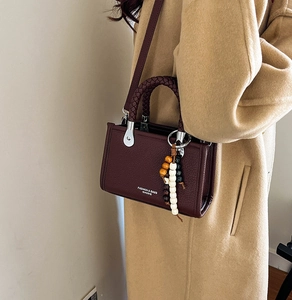 Detailansicht der weinroten Tasche mit Litschi-Muster, Flechtgriff und Holzperlen